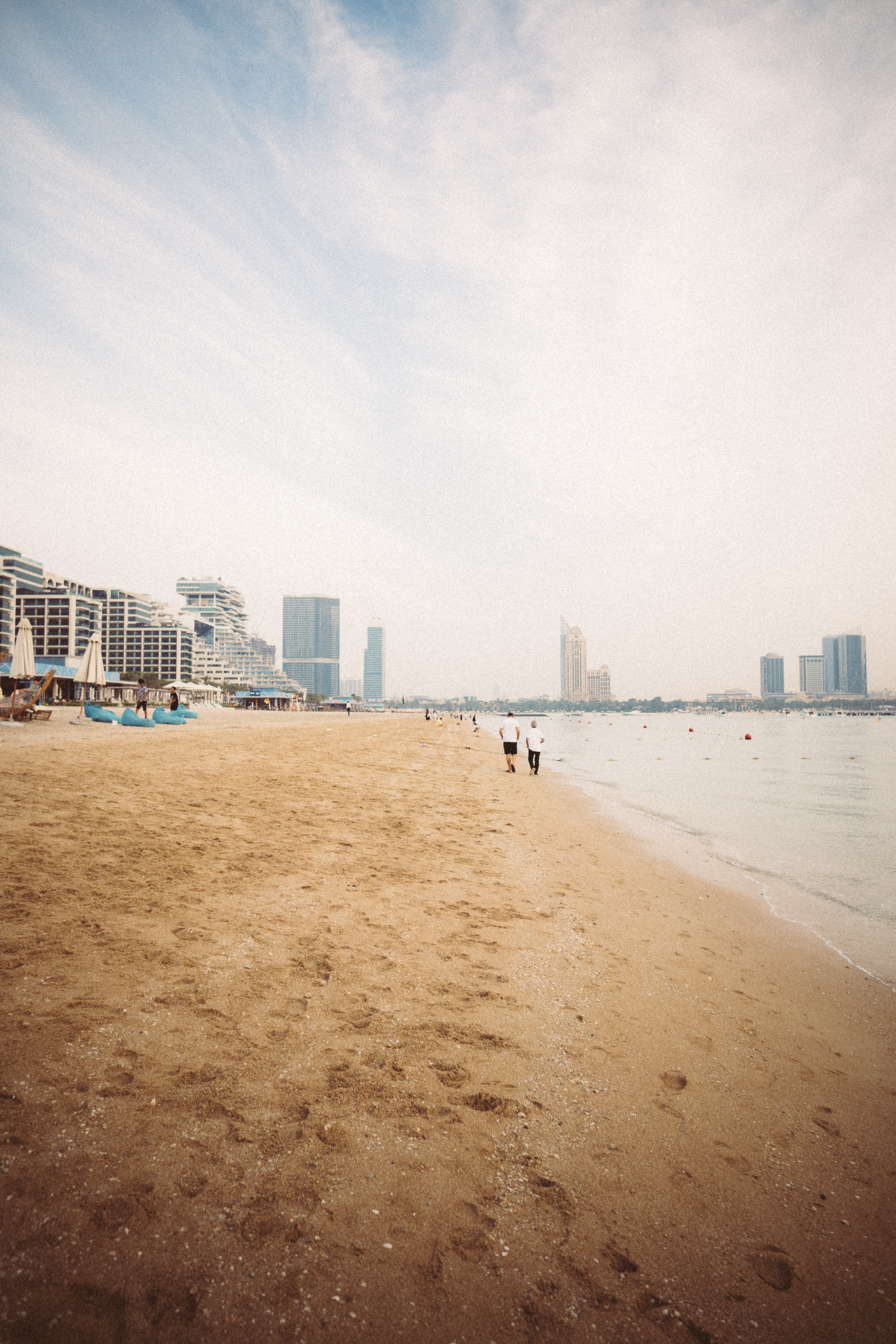 Plage de sable avec quelques promeneurs et des bâtiments sur le littoral de Dubaï.