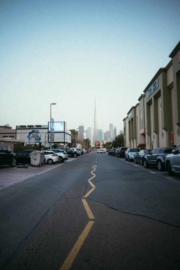 Vue sur Burj Khalifa depuis une rue locale de Dubaï, avec des voitures garées et des commerces.