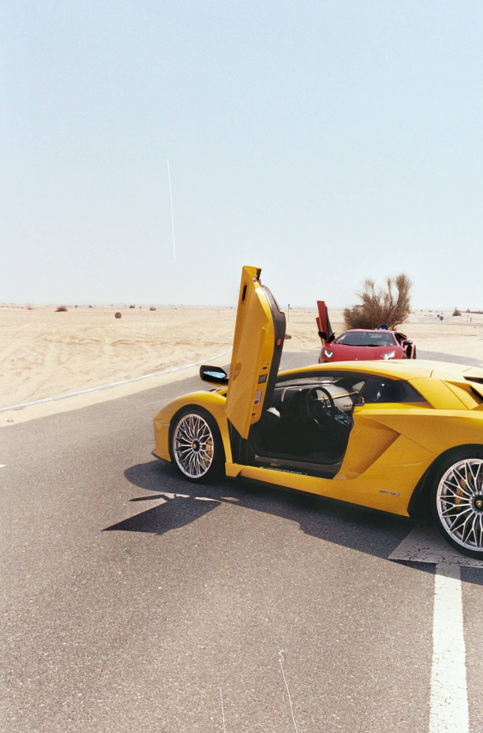 Deux Lamborghini avec portes papillon ouvertes sur une route traversant le désert de Dubaï.