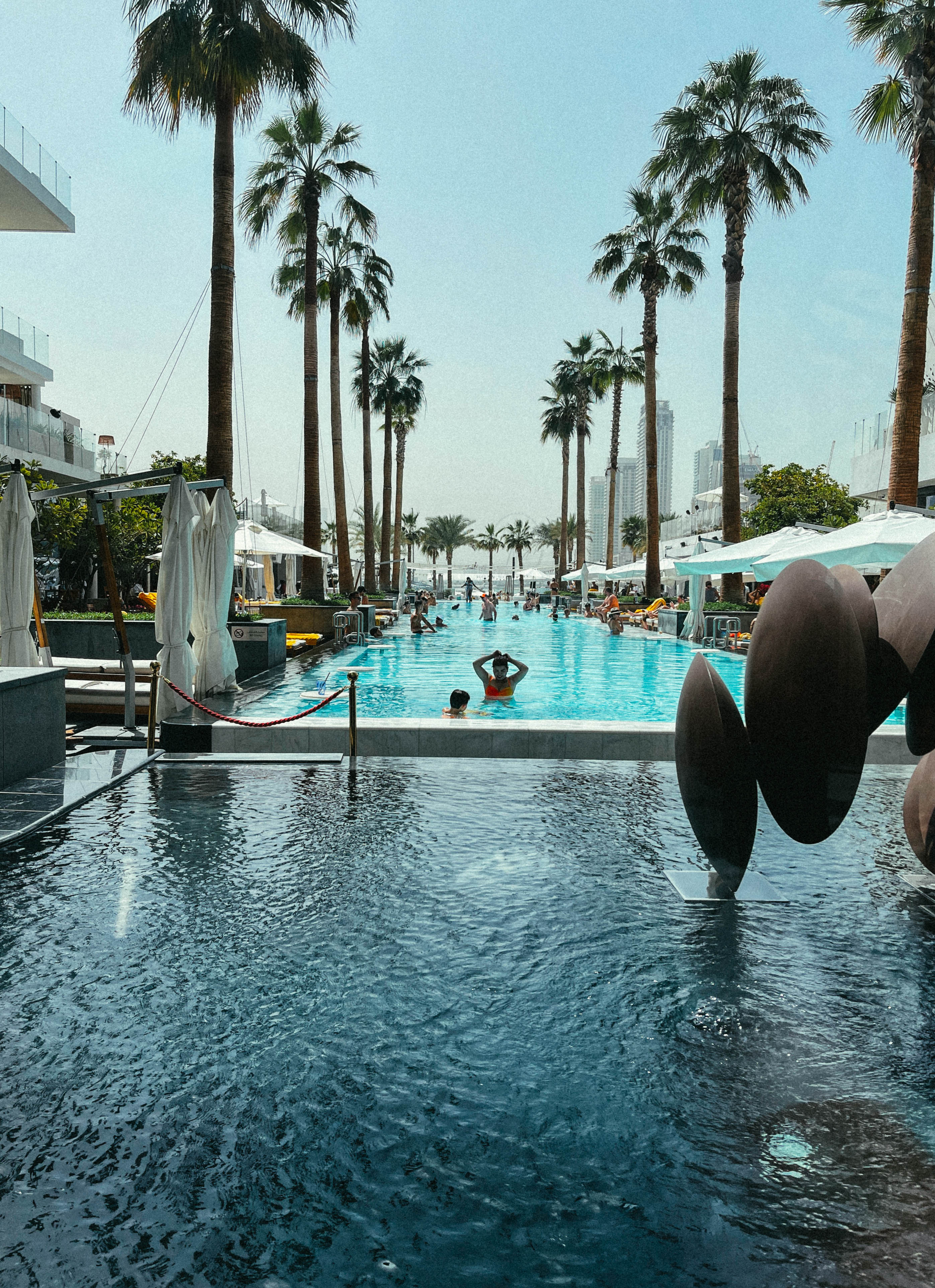 Piscine bordée de palmiers, de terrasses et de bâtiments à Dubaï.