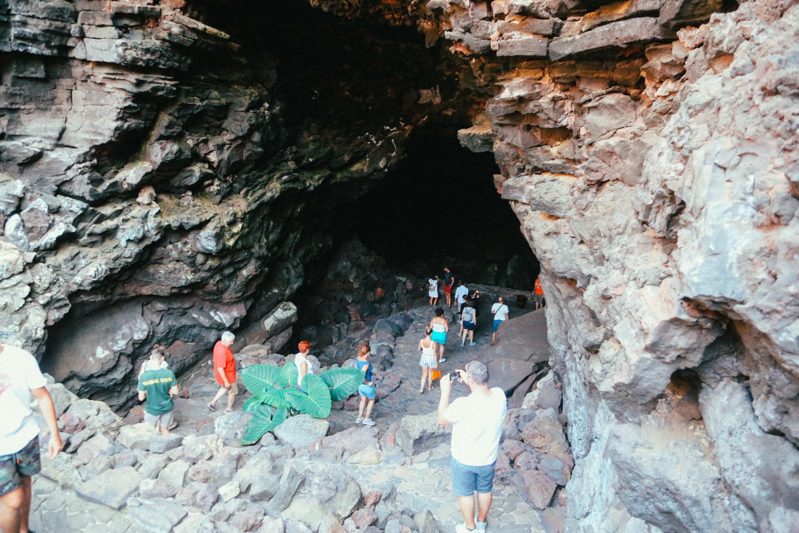 Entrée d’une grotte volcanique avec des visiteurs explorant l’intérieur.