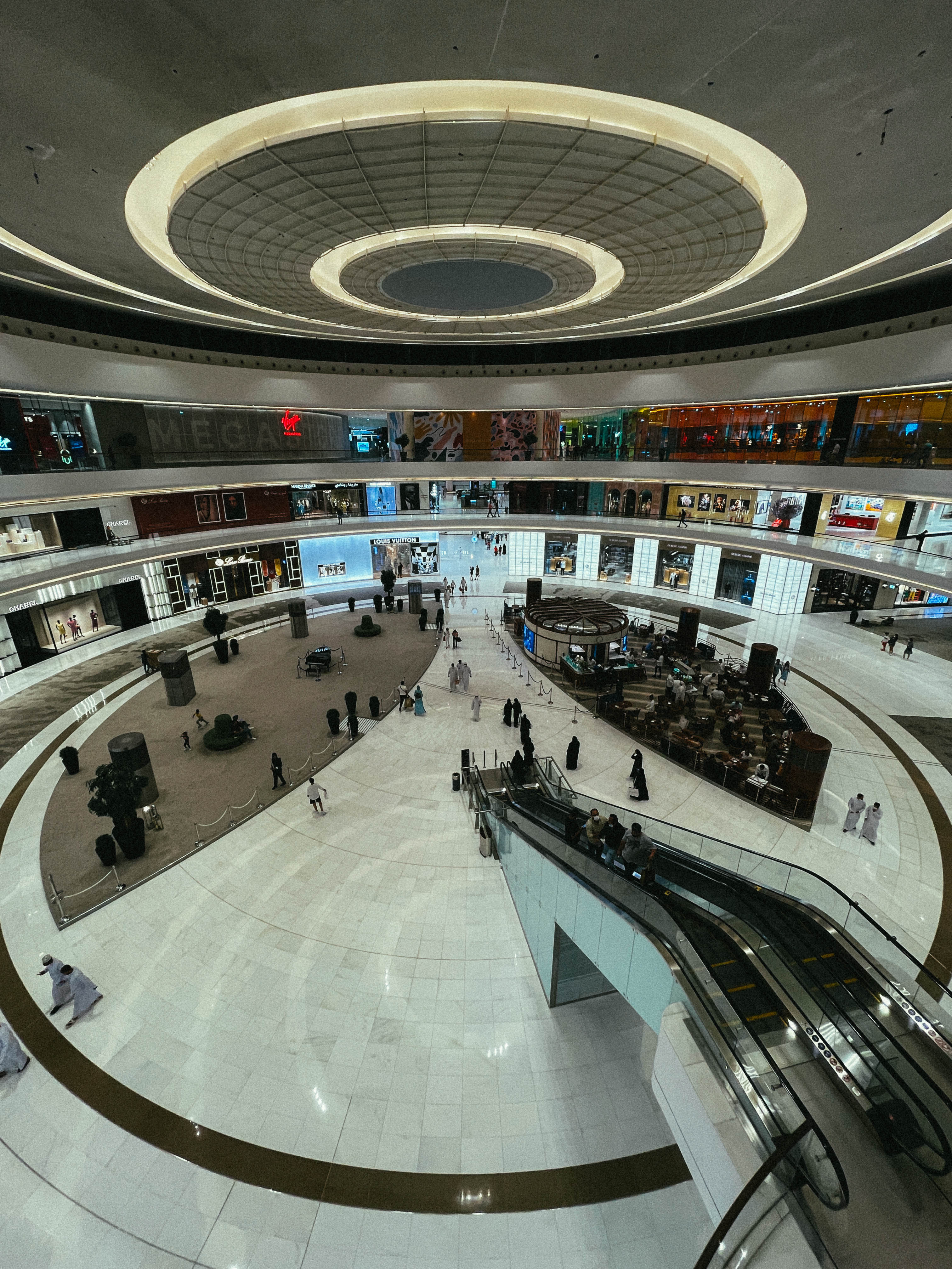 Étages et escalators d’un centre commercial, sous un grand plafond circulaire.