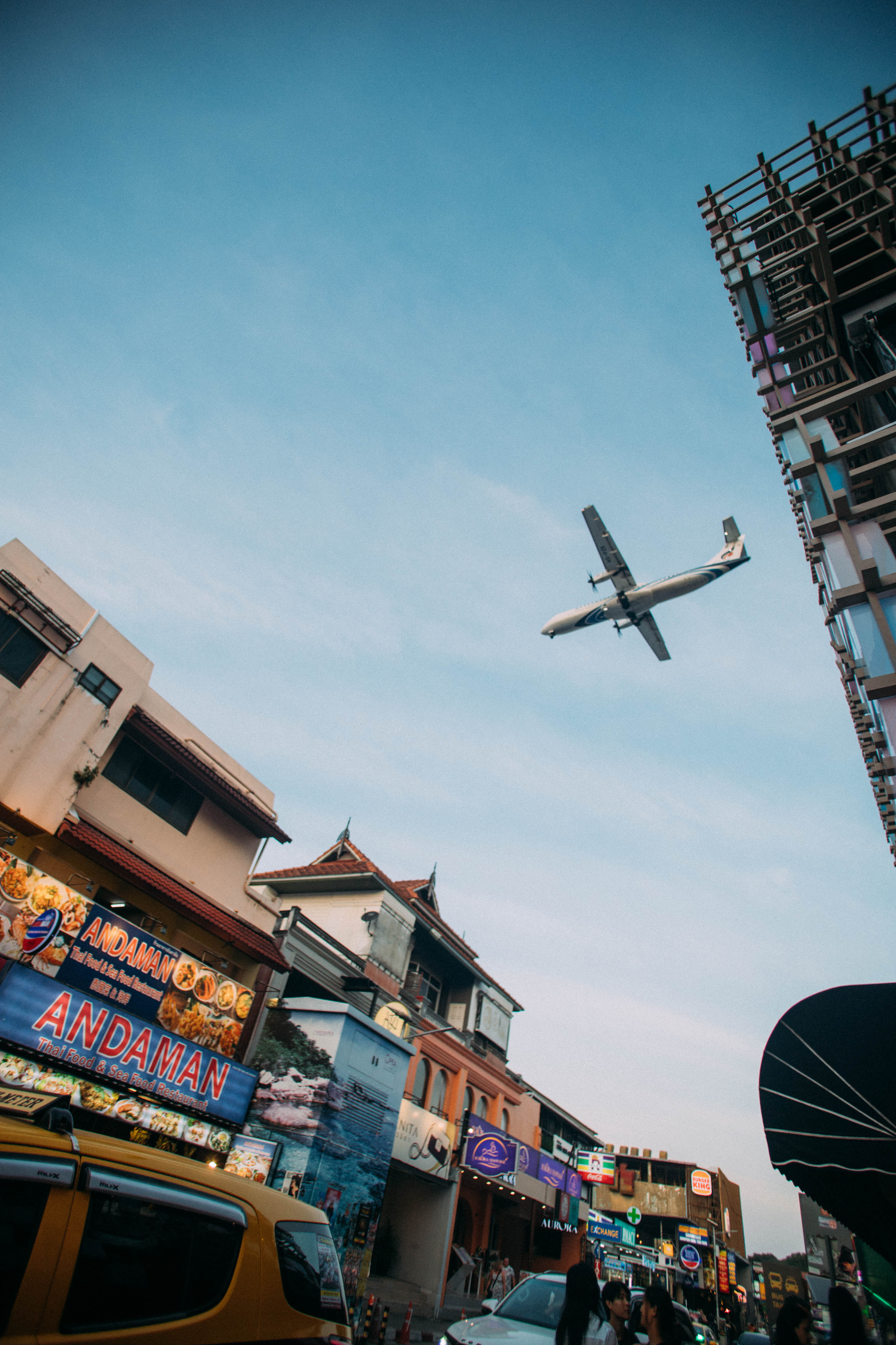 Un avion survole une rue bordée de bâtiments et d’enseignes à Koh Samui.