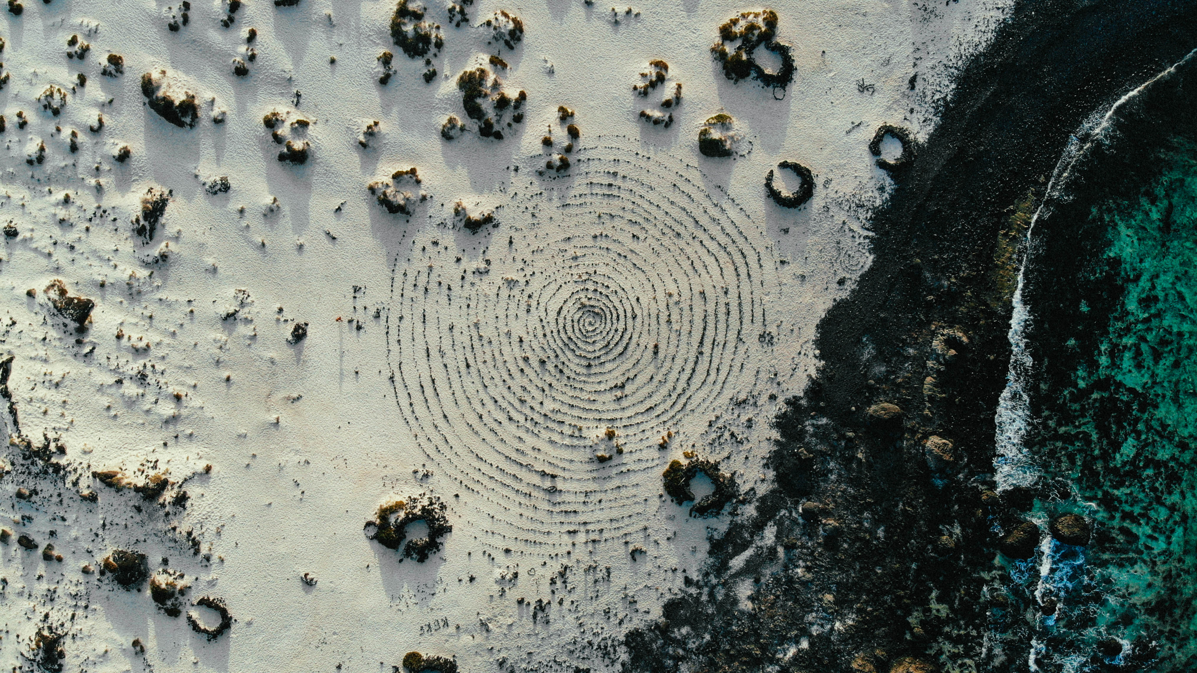 Vue aérienne d’une côte rocheuse de Lanzarote, avec un motif circulaire dans le sable.