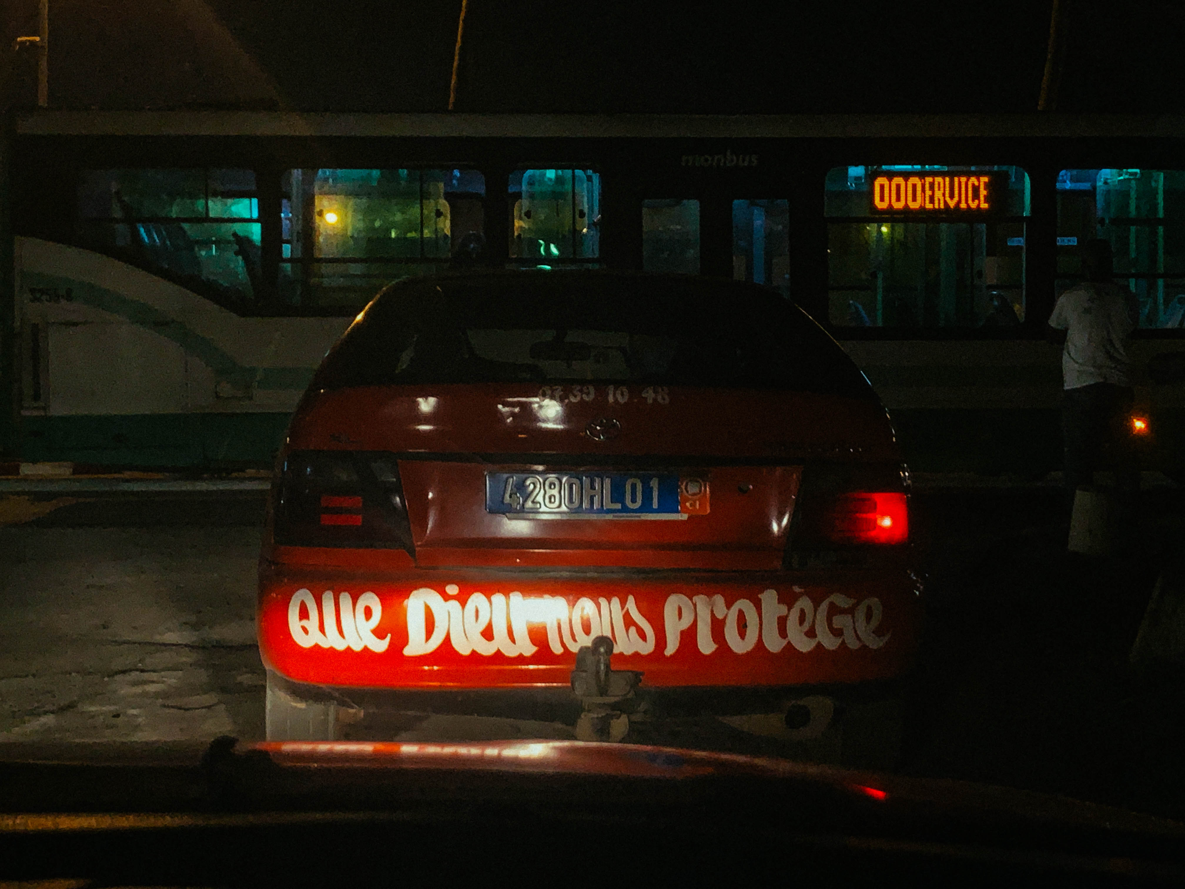 Taxi rouge photographié de nuit, avec un message peint à l’arrière.
