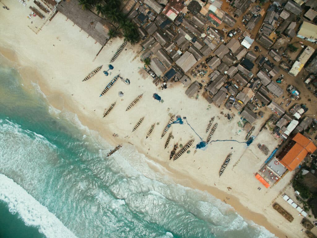 Vue aérienne d’un village de pêcheurs en Côte d’Ivoire, entre plages de sable fin et pirogues traditionnelles.