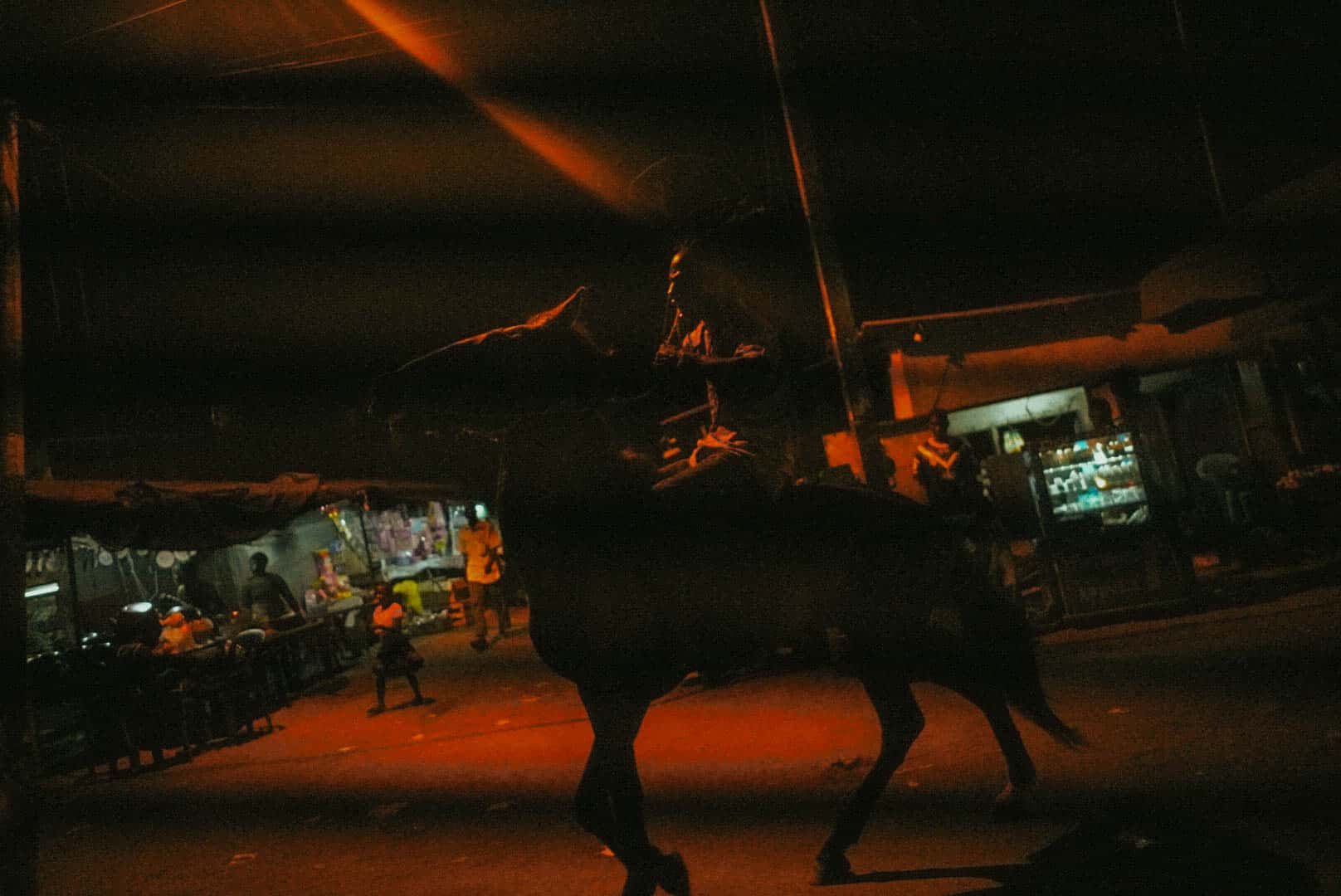 Un cavalier en pleine rue, sous les lumières orangées de la nuit en Côte d'Ivoire.