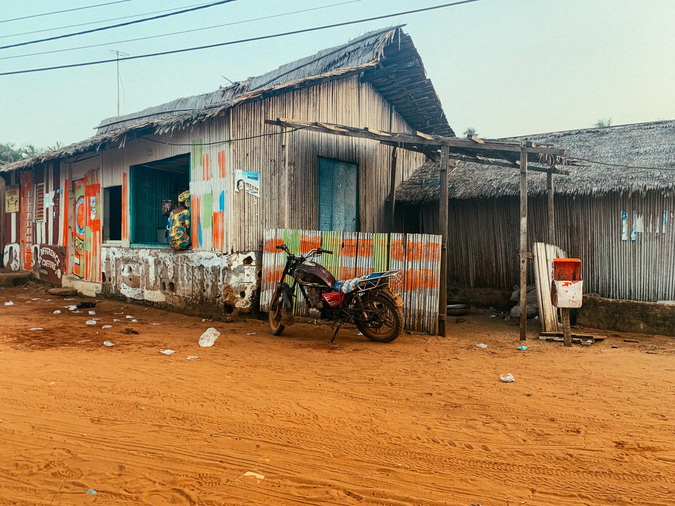 Une maison en tôle typique sur une route en terre rouge en Côte d'Ivoire.