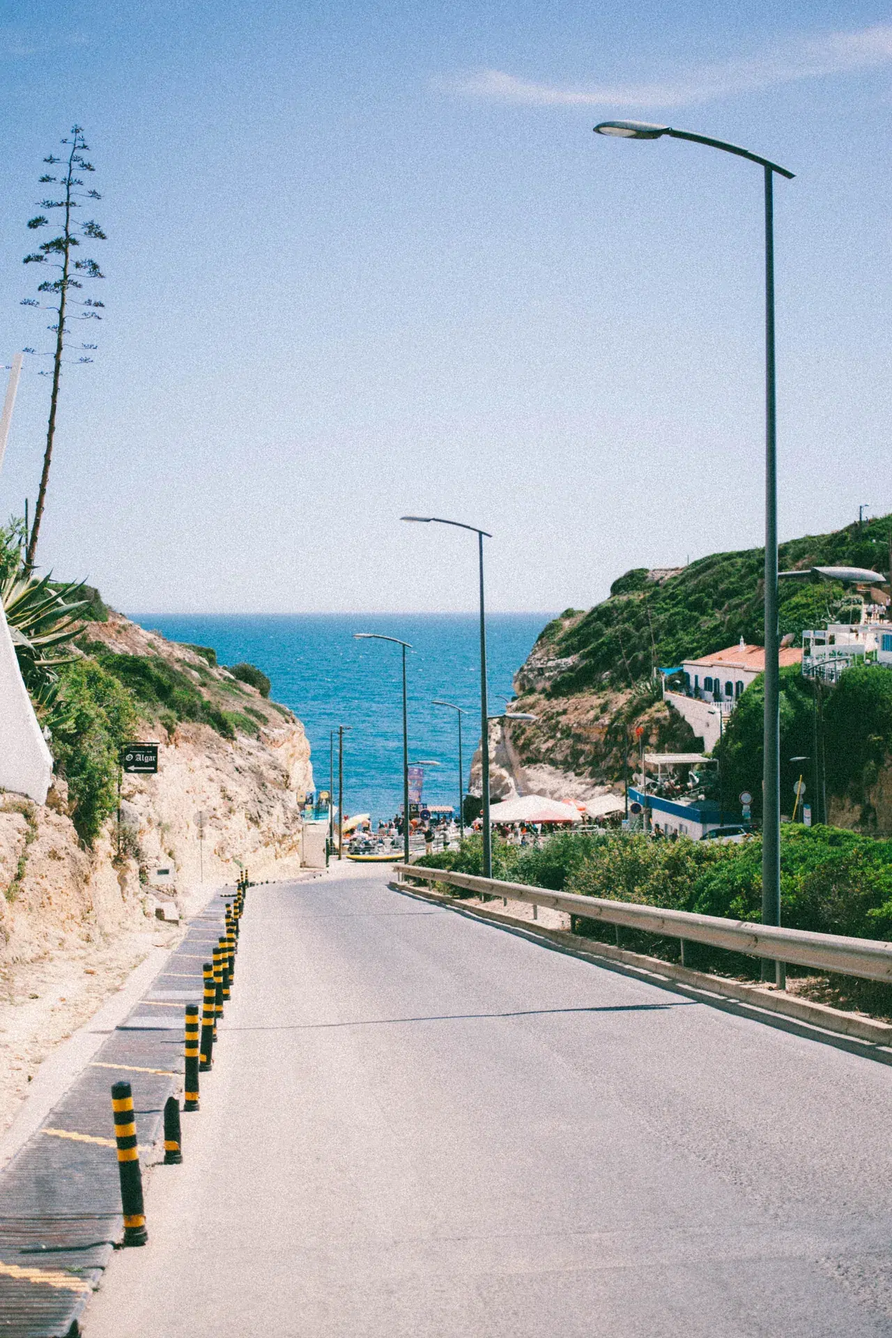 Rue en pente vers la mer à Benagil, avec végétation sur les côtés.