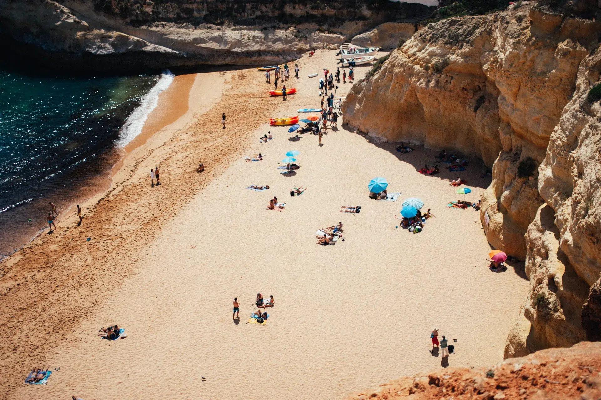 Plage de Benagil vue d’en haut, avec parasols, kayaks et falaises.